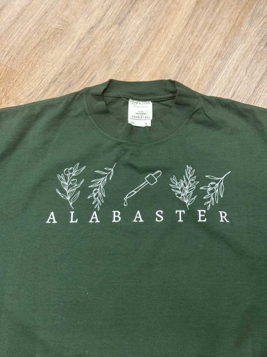 Green t-shirt with 'Alabaster' logo on a wooden surface